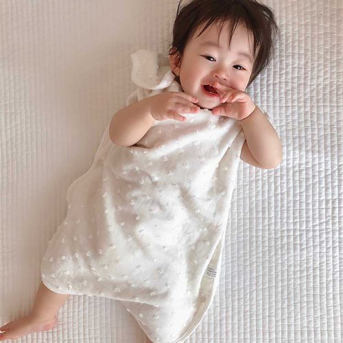Baby lying down wearing the Kontex Natural Dots sleeper in Ivory