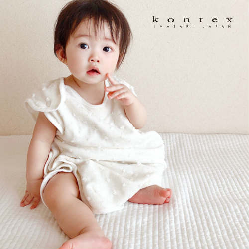 Baby seated wearing the Kontex Natural Dots sleeper in Ivory