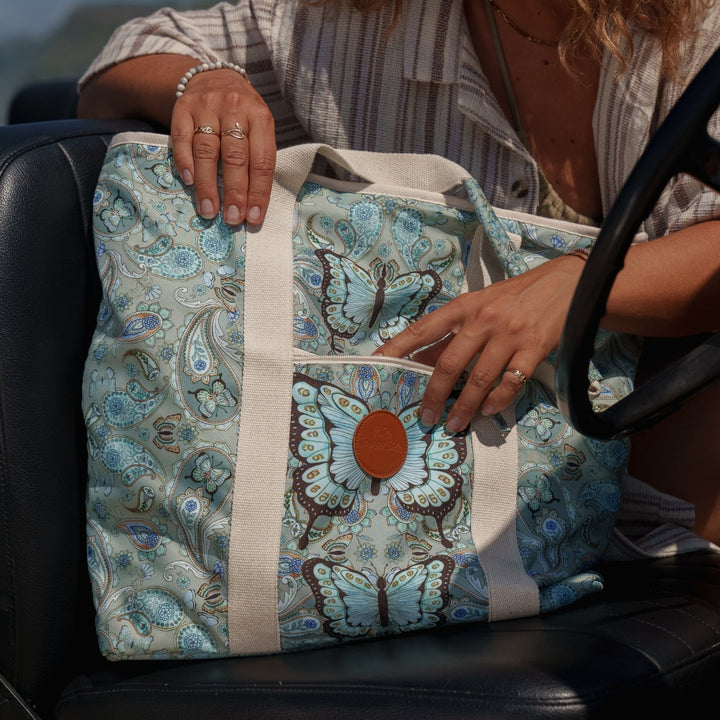 SomerSide Butterfly Effect 40L convertible beach bag with cream straps, shown beside a car