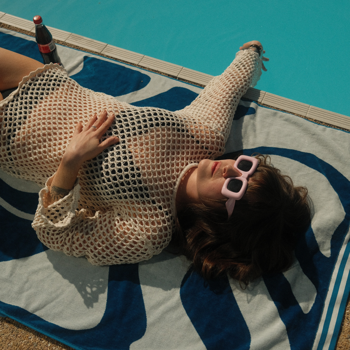 SomerSide Drift 600 GSM cotton beach towel in blue and bone white, with a person relaxing poolside